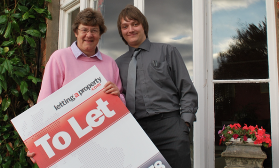 Female landlord with male tenant holding a lettingaproperty.com To-Let sign standing outside the property.